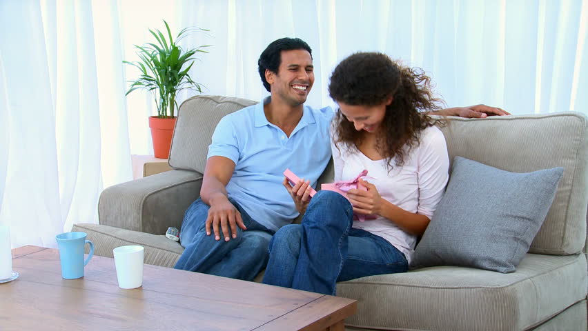 Woman opening the present that was offered by her husband on the sofa at home