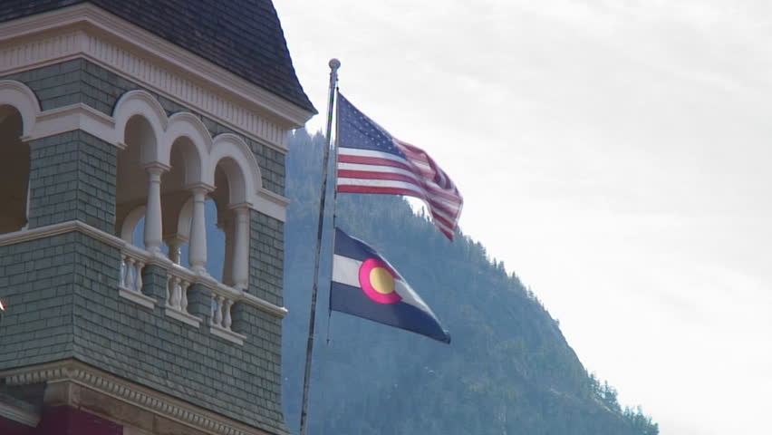 Colorado and US flags fly above old mountain town courthouse; Ouray Colorado; HD