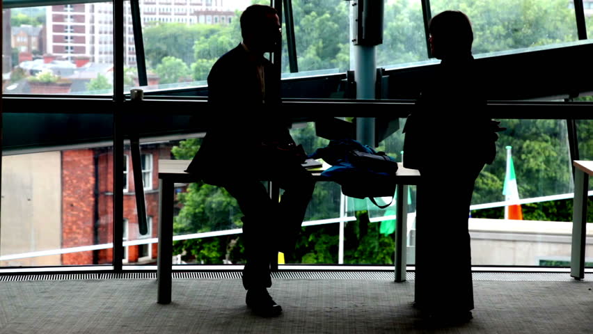  Business people silhouette, man sits at table near window and talks with woman.