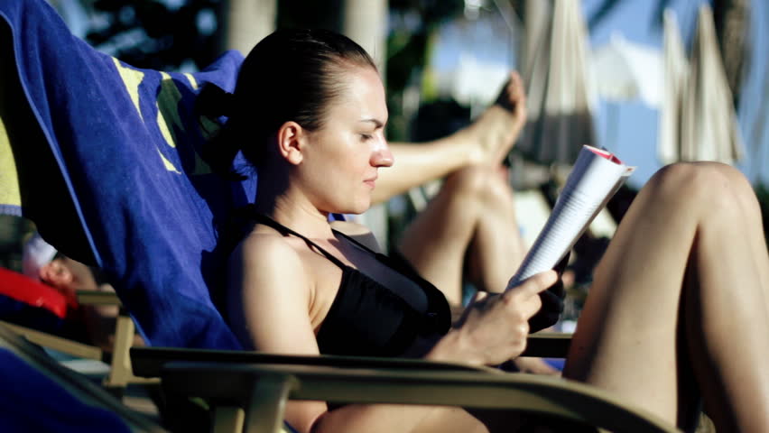 Young woman on sunbed reading newspaper