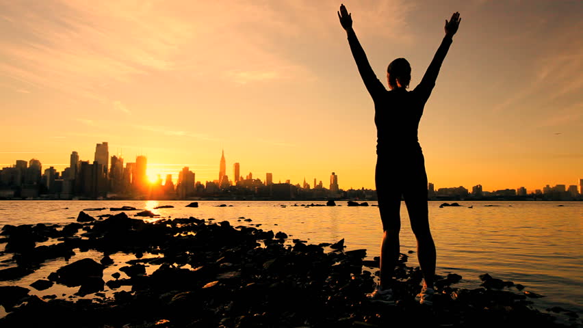 Female in silhouette saluting the challenge of a new day with a Manhattan skyline backdrop at sunrise