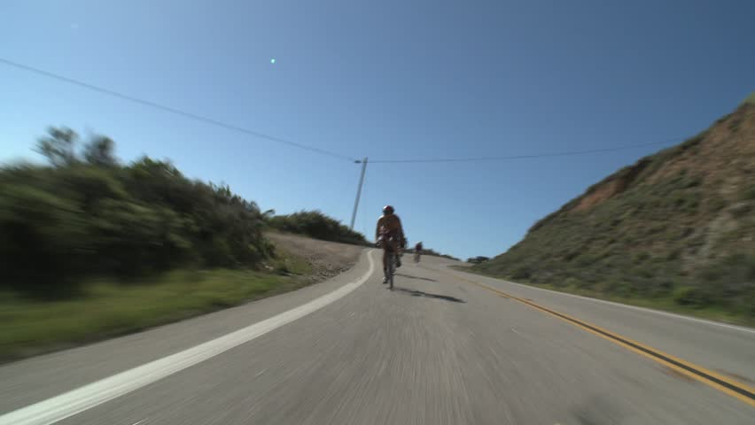 A group of bicyclists coast down winding coastal highway and encounter multiple curves.