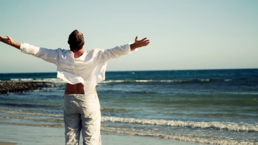 Man at the beach raising hands to the sky, freedom concept