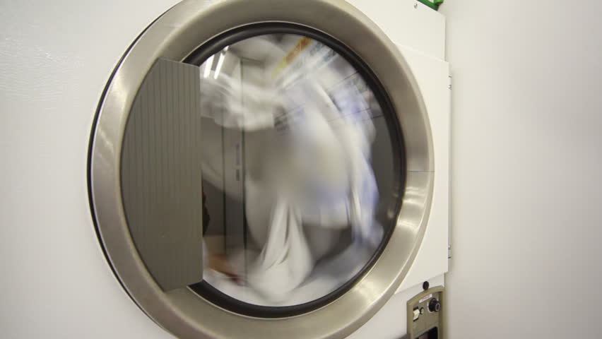 large washing machine, transparent glass door is spinning drum with laundry