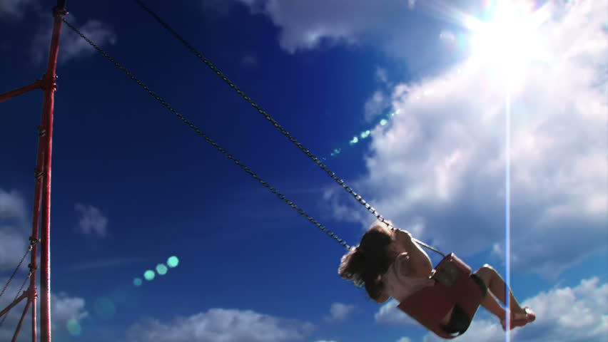 A young girl swings on a swing set in a playground  Low angle with the sky shown prominently.