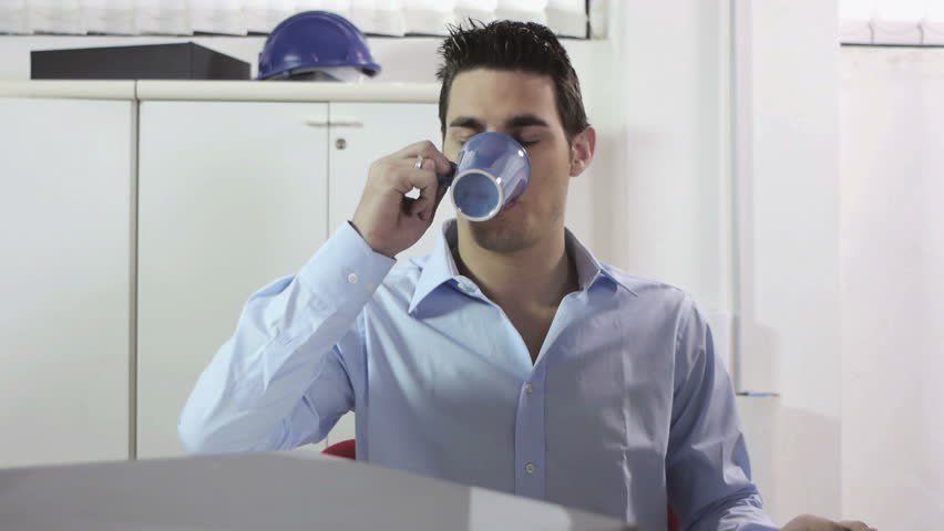 Tired adult caucasian businessman with paperwork and scrolls on desk, drinking coffee in office. Dolly shot