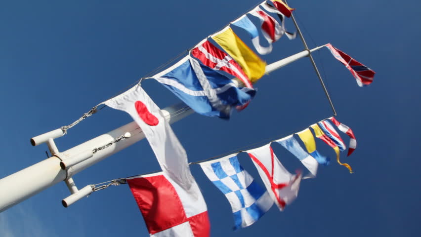 flags of different countries on mast and ropes flapping in wind against blue sky