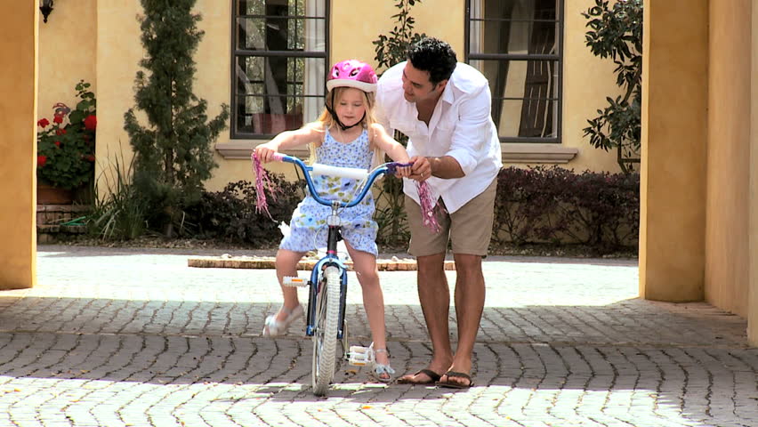 Asian father teaching his little blonde daughter to ride a bicycle