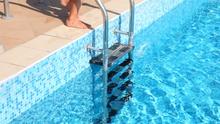 Boy in swimming cap descends in water in pool  by stair