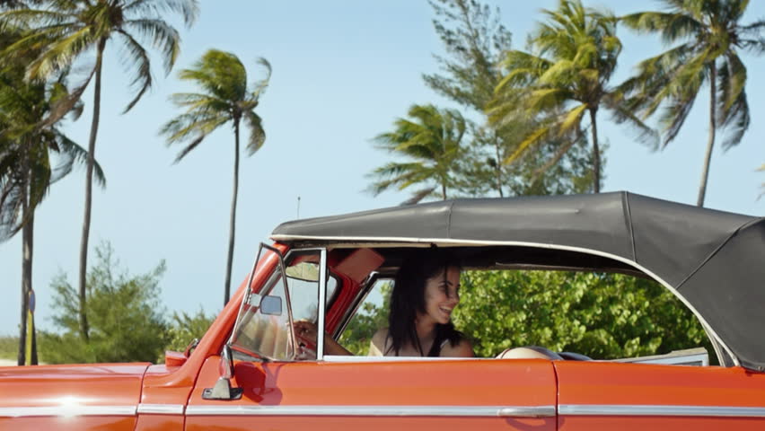 two beautiful young women laughing while pushing broken down red convertible vintage car