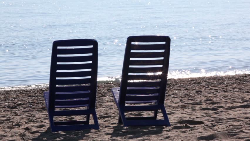 Two empty deckchairs stand on beach at sunny day, camera behind them