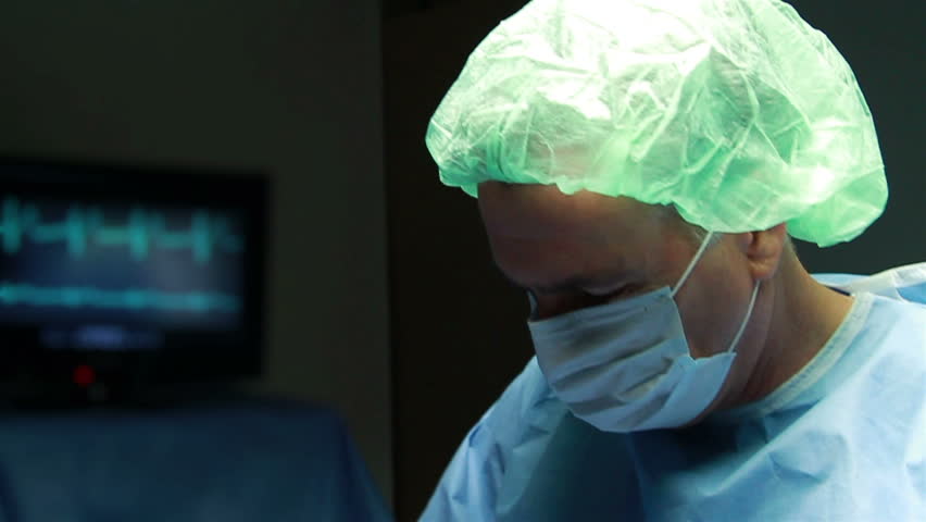 A surgeon reaches for defibrillator paddles when the heartbeat on the monitor goes to flat line, then he shows relief as it stabilizes.