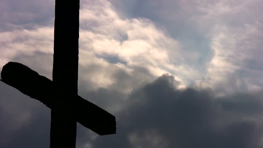 A large cross silhouetted against storm clouds at sunset.
