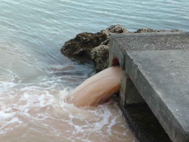 Sewage, waste or pollution gushing from a pipe into the sea next to a beach