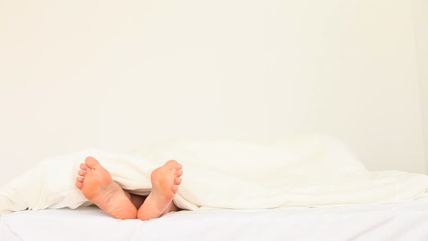 Wobbling toes under a sheet in a bed 