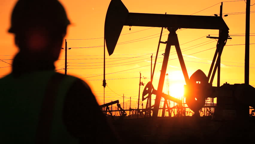 Female engineer by oil donkeys in perpetual motion producing crude oil  at sunset 