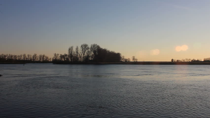 Large cargo barge passes by on the river Ijssel in a sunset at the end of the day.