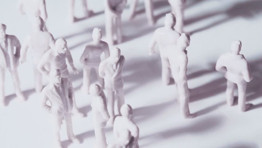 Group of little unpainted toy men and women stand and drop shadows, composition rotates, view from above