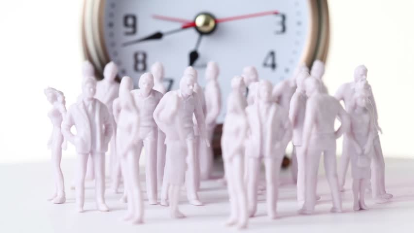 Group of little colorless toy men and women stand in front of big clock