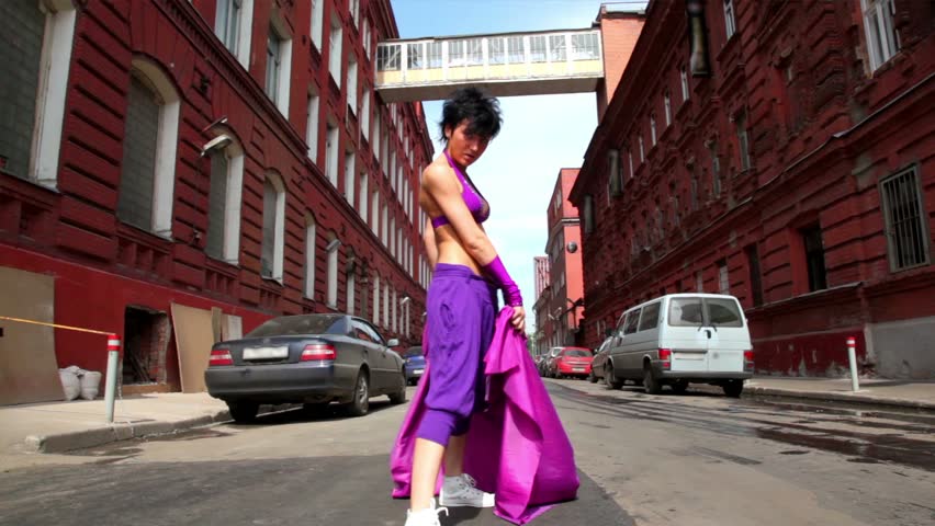 Girl dances in modern style with cloth on street between houses