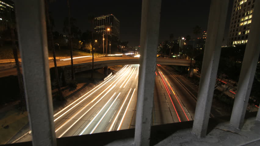 Vertical sliding time lapse shot behind bridge railing that slowly reveals a busy freeway at night.