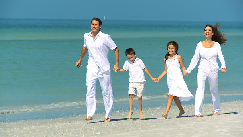 Happy young family having fun on vacation skipping outdoors on the beach filmed at 60FPS