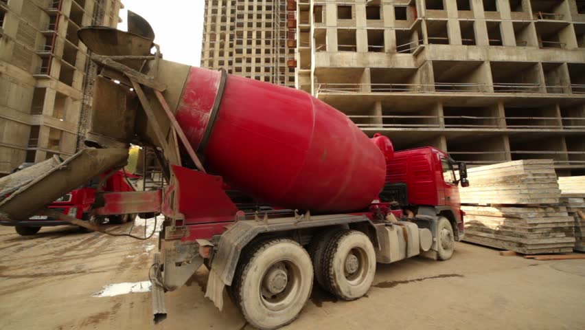 Concrete mixer stand at building place, truck full of sand arrives, workers work around