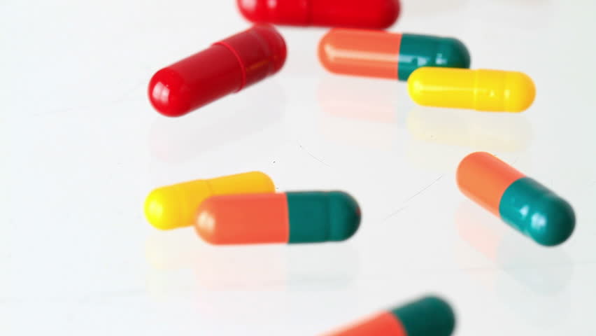 drugs/capsules/medicine laying out on table with open pharmacy vial and cap. Camera pans forward