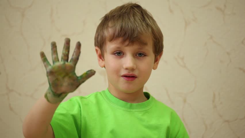 Boy in green T-shirt waves his right palm smeared with coloured paints
