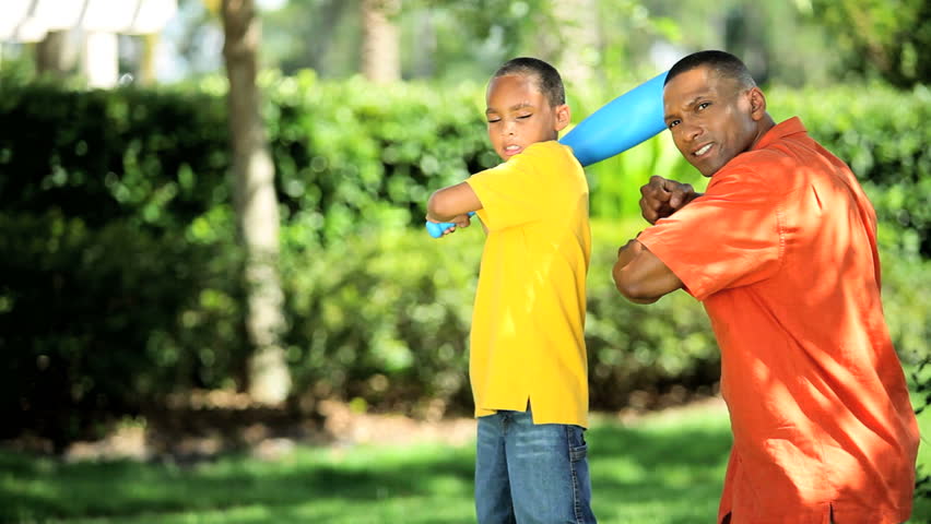 Young african american father teaching his son how to swing a baseball bat