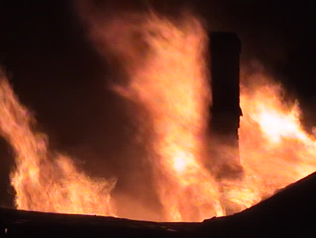Flames coming from the roof of a structure and surrounding the chimney.