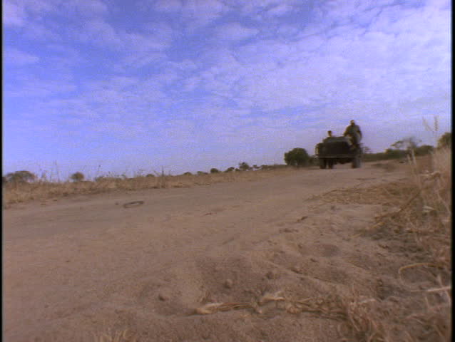 A group of men sit in an open air Jeep traveling on a sandy road in Kenya.