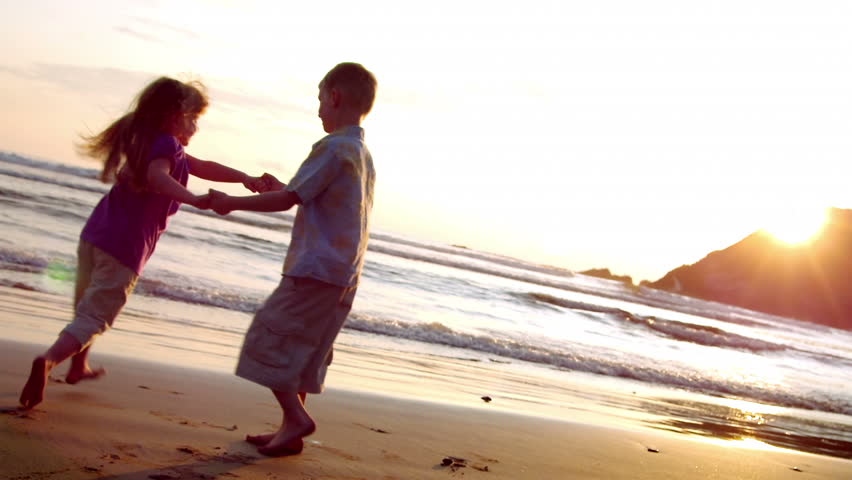 Grandparents and grandchildren enjoy a day at the beach.  Their activities include using a computer, walking on the beach, watching the sunset, having a drink, holding hands, and sharing an embrace.