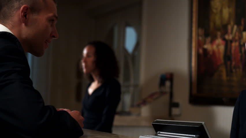 A young businessman flirts with the hotel staff as he checks in for the night.