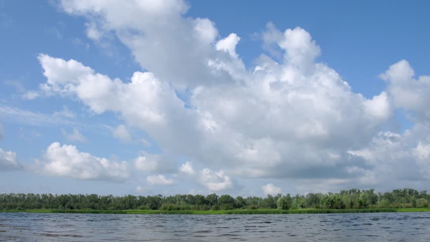 Narrow stripe of forest between cloudy sky and Volga River, view from coast, time lapse 