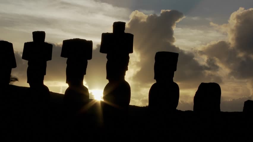 The sun peeks out from behind an Easter Island statue.