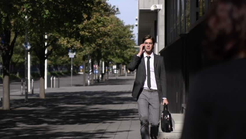 Young businessman talking on mobile phone and walking in the street. Slow motion