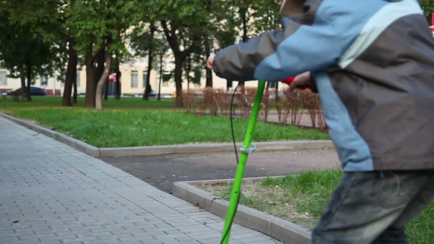 Boy ride on scooter at tiled road in park at autumn day