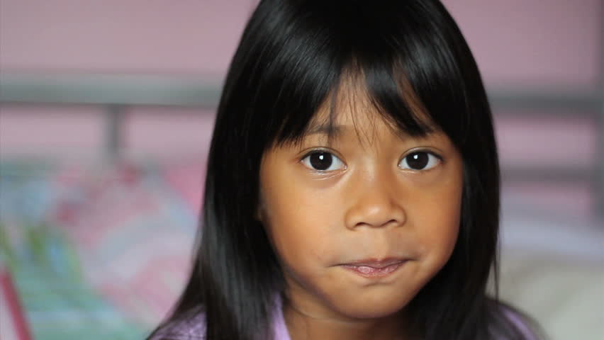 A cute little 5 year old Asian girl wiggles her first loose front tooth.