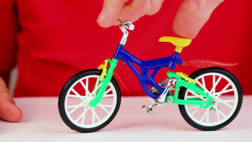 Boy play with toy bike, rotates handlebars, try to make trick but fall