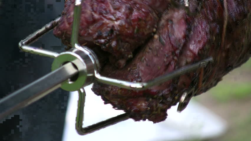 detail of savory meat roasting on a spinning rotisserie with smoke, dripping juices, and flame reflections