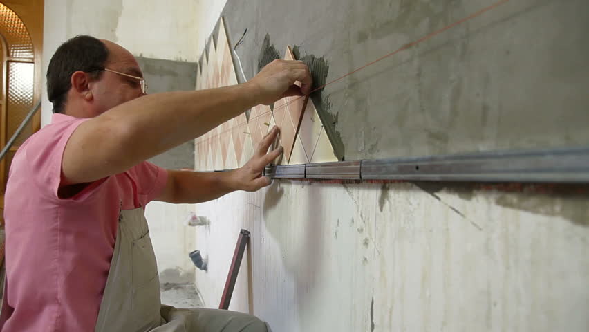 man applying ceramic tile to a Kitchen wall. Medium Shot, Side View
