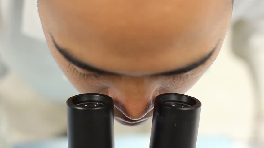 Researcher from above in a labcoat looks into a microscope and adjusts the eye piece.