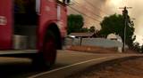 Medium shot of fire trucks racing down a small town street toward a wildfire.
