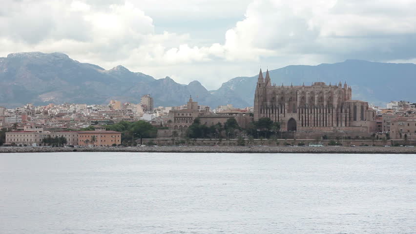 Palma Mallorca Majorca Cathedral Basilica and Palma City across the beautiful and rainy bay and harbor. Pan from slow moving ship. Storm shrouded mountains in distance past city.