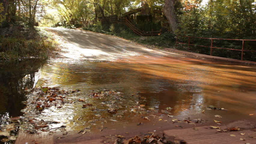 The waters of Oak Creek in Sedona rush quickly over a concrete road area as the beautiful fall colors and sunlight are reflected in the stream.