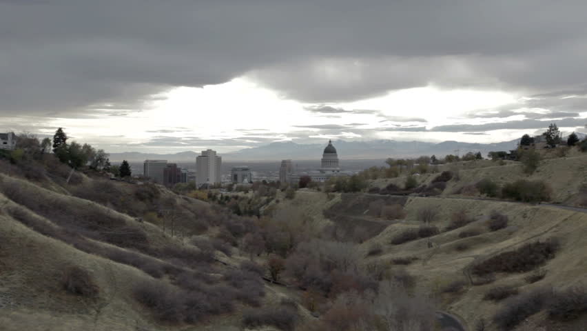 Utah State Capital from mountain canyon looking past dome into valley and Salt Lake City. Normal haze from city. Traffic on mountain road leading to building.