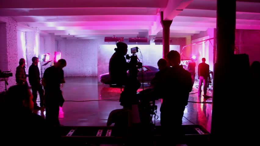 operator with videocamera moves on cart on rails, film crew is illumination preparation