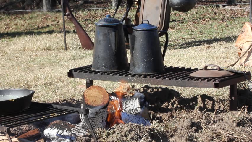 Old time black kettles sitting on a cast iron rack over a campfire in daytime
