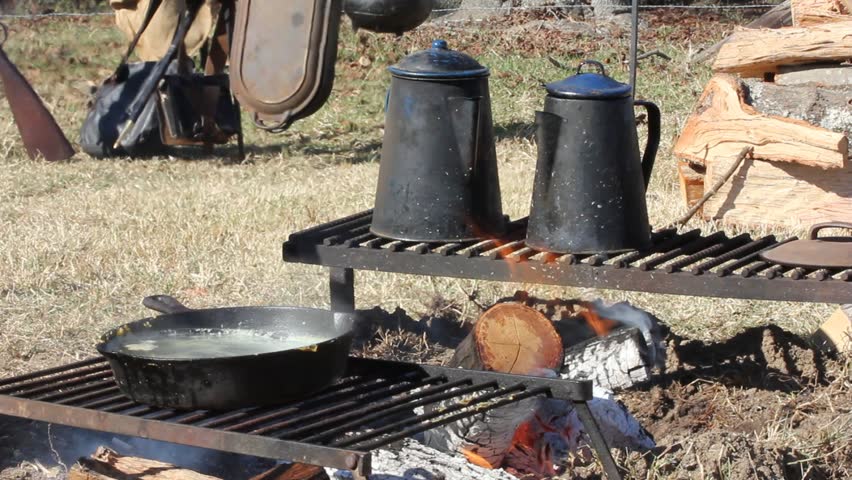 Civil War era cooking setup with kettles and skillet on racks with campfire